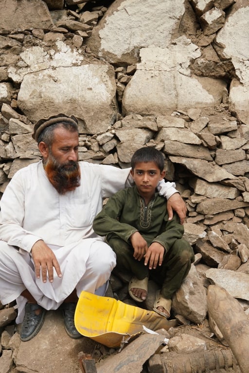 En pappa och son sitter bland stenar efter en jordbävning i Afghanistan 2025.
