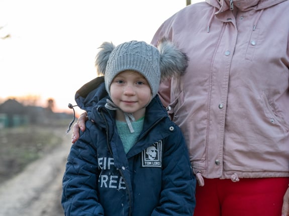 En familj i Ukraina står på en väg med sönderbombade hur.