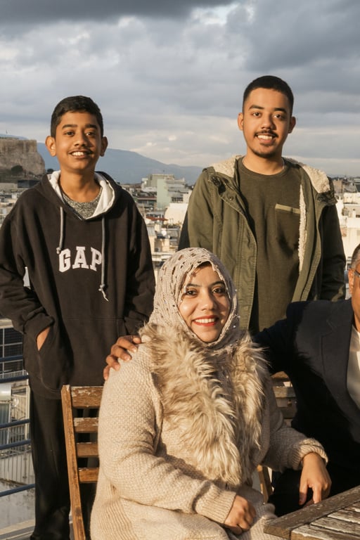 En familj med fyra personer tittar in i kameran och ler. I bakgrunden syns greklands huvudstad Aten.