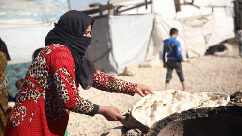 En kvinna i ett flyktingläger lagar bröd över en eld.