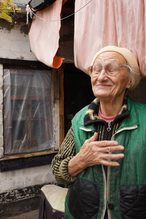 Nadiia, en äldre kvinna i Ukraina, står framför sitt enkla hem.