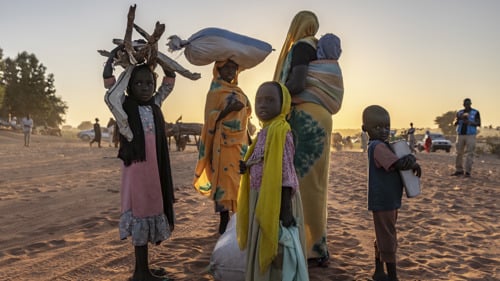 Kvinnor och barn på flykt från Sudan står i öknen med packning för att söka skydd i Tchad.