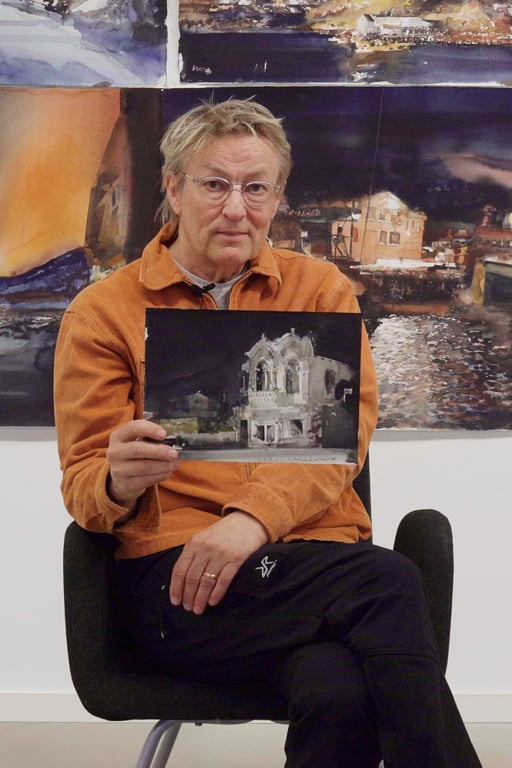 Lars Lerin sitter på en pall och visar upp en tavla.