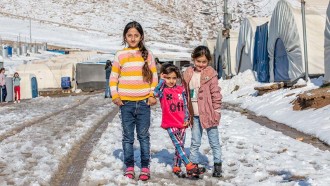 Tre flickor står framför sitt tält i ett flyktingläger i Irak.