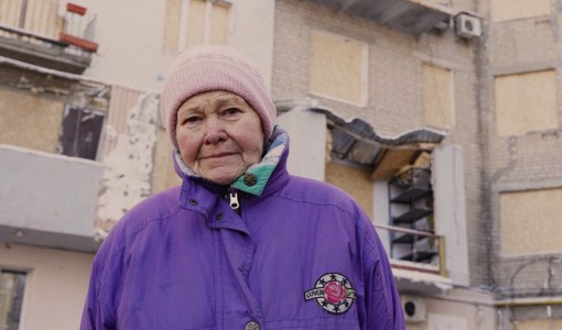 82-åriga Valentyna står utanför sitt bostadshus i Kharkiv. Huset träffades i ett luftangrepp i januari 2024.