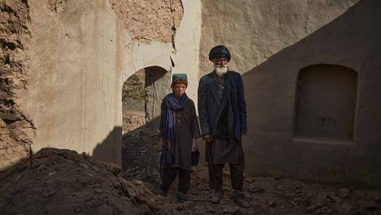 Sayed Mohammad* och hans son står vid sitt förstörda hem i Marja, södra Afghanistan.