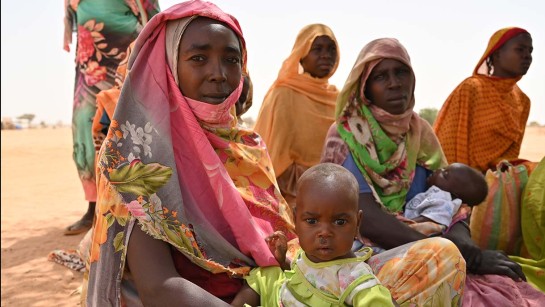 Kvinnor sitter i en öken på flykt från Sudan.