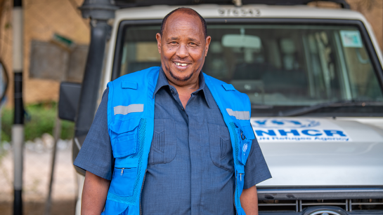 UNHCR:s chaufför Ahmed Abdinoor står framför en UNHCR-bil. 