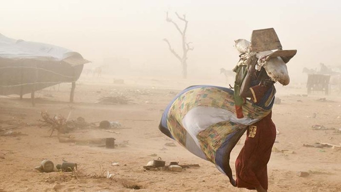 En sandstorm sveper genom det karga landskapet. En kvinna har flytt våldet i Sudan, hon kämpar för att överleva.